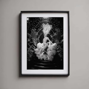 May include: A black and white photograph of a woman in a feathered costume performing on stage. She is wearing a sequined dress and a large feathered headdress. The stage is decorated with a large, ornate backdrop.