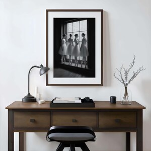 May include: A framed black and white photograph of four ballerinas in white tutus, standing by a window. The photograph is displayed above a wooden desk with a black lamp, candles, and a decorative tray.