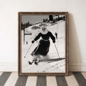 Peut inclure: Tirage encadré en noir et blanc d'une religieuse skiant sur une pente enneigée. La religieuse porte une longue robe noire, une guimpe blanche et des lunettes de soleil, utilisant des bâtons de ski. La photo vintage est dans un cadre marron décoratif.