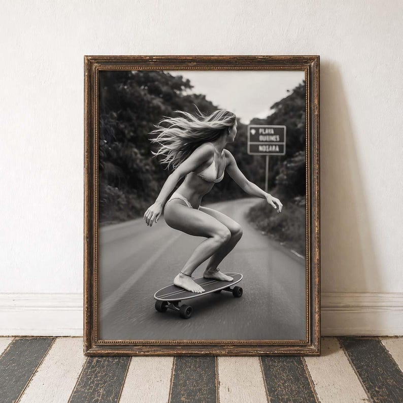 Peut inclure: Tirage encadr&eacute; en noir et blanc d'une personne faisant du skateboard sur une route. La personne porte un bikini et a de longs cheveux. Un panneau routier est visible en arri&egrave;re-plan. L'impression est dans un cadre marron.