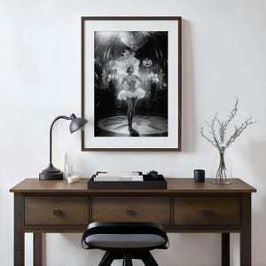 May include: Black and white framed print of a woman in a white tutu and feathered headdress, standing on a stage. The print is displayed on a dark wood desk with a black lamp, candles, and a decorative tray.