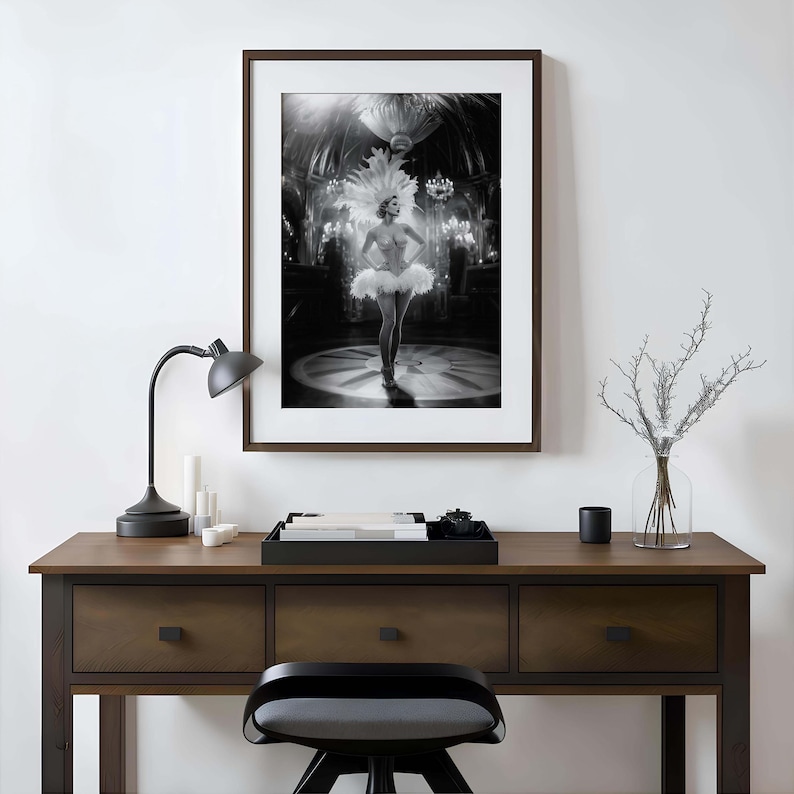 May include: Black and white framed print of a woman in a white tutu and feathered headdress, standing on a stage. The print is displayed on a dark wood desk with a black lamp, candles, and a decorative tray.