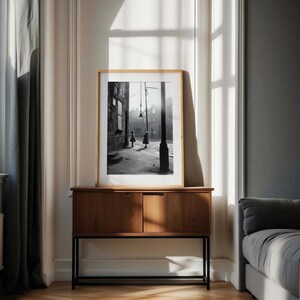 May include: A black and white photograph of two children walking down a street in a city. The photo is framed in a wooden frame and is hanging on a wall above a wooden cabinet.