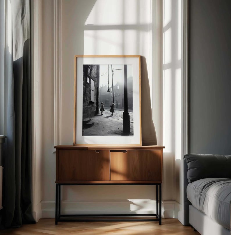 May include: A black and white photograph of two children walking down a street in a city. The photo is framed in a wooden frame and is hanging on a wall above a wooden cabinet.