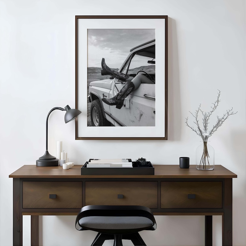 Pu&ograve; includere: Stampa incorniciata in bianco e nero di gambe e stivali da cowboy che sporgono da un camion bianco d'epoca. La foto &egrave; ambientata su uno sfondo di cielo nuvoloso e colline, evocando un senso di avventura e libert&agrave;.