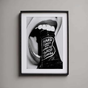 Puede incluir: Impresión enmarcada en blanco y negro que muestra una boca mordiendo una botella oscura. La botella tiene el texto "HARD times are some of the BEST times" en escritura blanca. Una audaz pieza de arte mural.