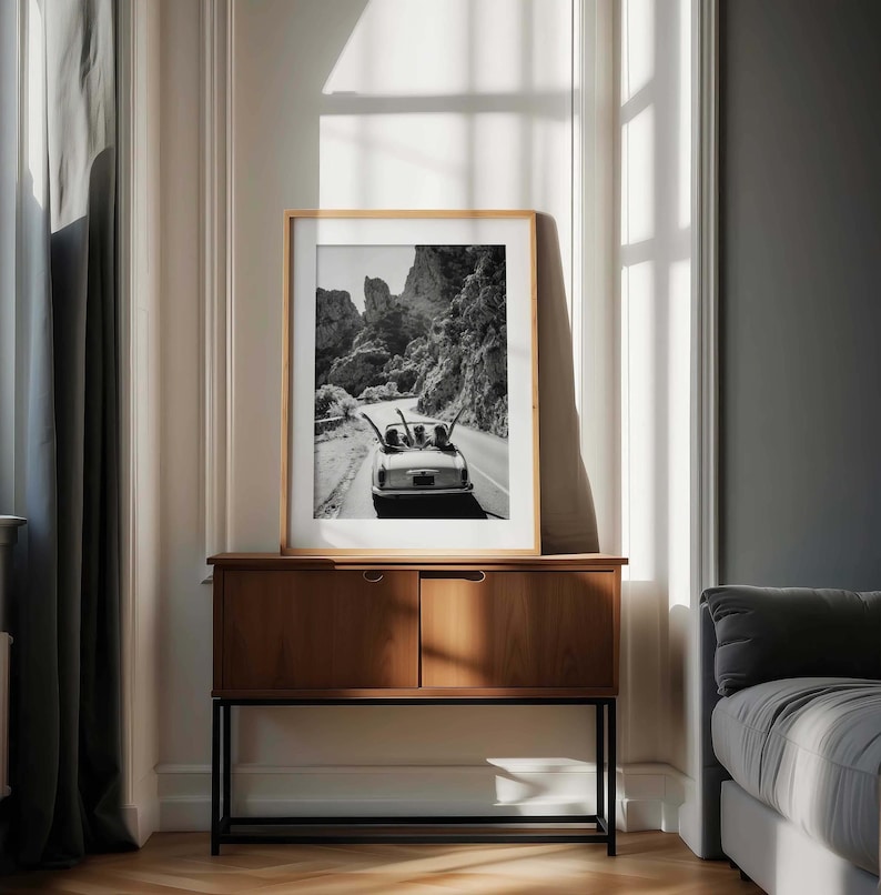 Puede incluir: Fotograf&iacute;a en blanco y negro enmarcada de un coche descapotable cl&aacute;sico en una carretera sinuosa de monta&ntilde;a. La imagen se muestra en un mueble de madera con marco de metal negro.