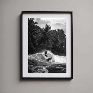May include: A black and white photograph of a surfer riding a wave in front of a lush tropical forest. The surfer is wearing a wetsuit and is riding a surfboard.