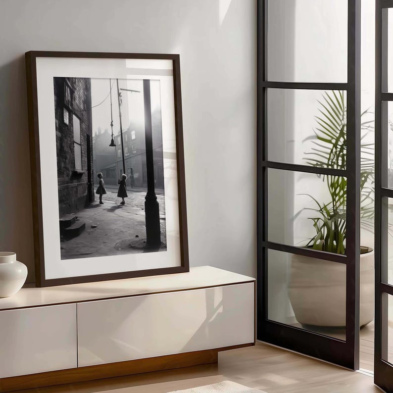 May include: A black and white photograph of two children walking down a narrow street. The photo is framed in a dark wood frame and is displayed on a white entertainment center.