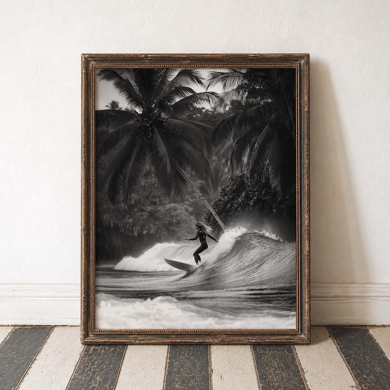 May include: Black and white framed print of a surfer riding a wave. The image features a surfer in silhouette, set against a backdrop of palm trees and a crashing wave. The frame is a dark, ornate wood.