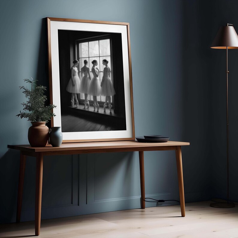 May include: A framed black and white photograph of four ballerinas in white tutus and pointe shoes, standing by a window. The photograph is displayed on a wooden table with a vase and plant. The room has blue walls and a floor lamp.
