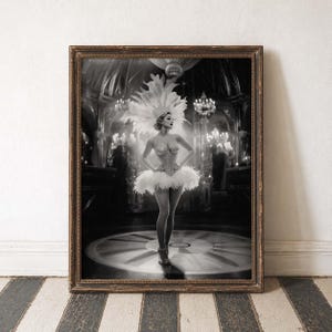 May include: Black and white framed print of a woman in a feathered costume, standing on a circular stage. The woman wears a corset, tutu, and headdress, with a backdrop of a chandelier-lit room. The print is in a brown wooden frame.