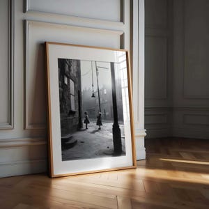 May include: Black and white photograph of two girls playing in a street with a lamppost in the background.