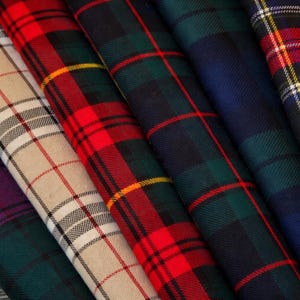 Puede incluir: Primer plano de telas escocesas plegadas en varios colores. Las telas muestran patrones de cuadros tradicionales en tonos de rojo, verde, azul marino, morado y beige. La imagen resalta la textura y el detalle de los materiales tejidos, para ropa o decoración.