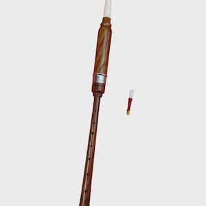 Puede incluir: Una gaita de madera con boquilla blanca y banda plateada. La gaita tiene un acabado marrón oscuro con una base roja. También se ve una lengüeta separada.