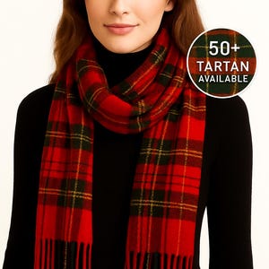 May include: A red tartan scarf with black and yellow detailing. The scarf is fringed and worn around the neck. A circular graphic in the image states "50+ Tartan Available".