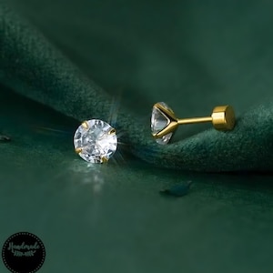 Könnte beinhalten: Ein Paar goldene Ohrstecker mit klaren runden Zirkonia-Steinen.