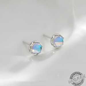 以下が含まれることがあります： 繊細な花の形をしたデザインに、虹色の青と白の石がセットされた、銀製のイヤリングのペアです。