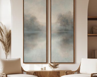 May include: Two framed abstract landscape paintings with a muted color palette of blues and grays. The paintings depict a misty lake scene with trees in the background. The paintings are hung on a white wall above a wooden console table.