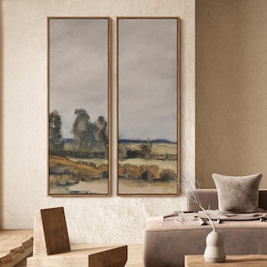 May include: Two framed landscape paintings with a muted color palette. The artwork depicts a field with a fence, trees, and a cloudy sky. The frames are a warm brown color, complementing the neutral tones of the artwork.