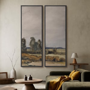 May include: Two framed landscape paintings. Each features a muted color palette with a field, trees, and a cloudy sky. The frames are dark, and the artwork evokes a sense of calm and nature.