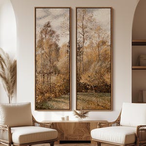 May include: Two framed landscape paintings depict a forest scene with trees in shades of gold, brown, and green. The artwork has a vintage aesthetic, with a soft, muted color palette. The paintings are displayed above a wooden cabinet.