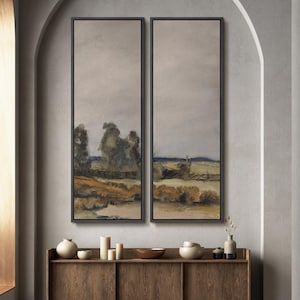 May include: Two framed landscape paintings with a muted color palette of gray, brown, and blue. The artwork depicts a rural scene with trees, fields, and a fence. The paintings are displayed above a wooden cabinet with decorative items.