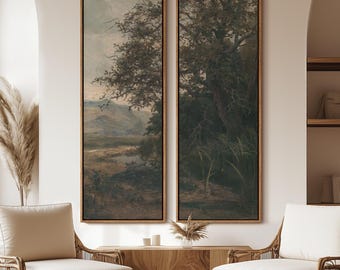 May include: Two framed landscape paintings with a vintage aesthetic. The artwork depicts trees and a body of water in muted tones of green, brown, and gray. The frames are a warm, natural wood color. The paintings are displayed above two wicker chairs.