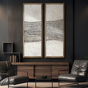 May include: Two abstract paintings in black and white with a textured background. The paintings are framed in a light wood frame and are hanging on a dark wall.