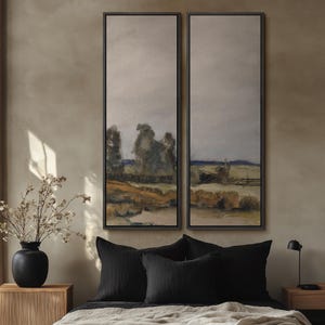 May include: Two framed landscape paintings with a muted color palette of beige, gray, and brown. The artwork depicts a rural scene with trees and a fence. The paintings are displayed above a bed with black pillows and a wooden nightstand.