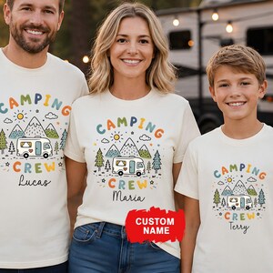 May include: Three people wearing cream-colored t-shirts with a camping-themed graphic. The design includes a camper, mountains, trees, and the text "CAMPING CREW" with a custom name below. The shirts are paired with blue jeans.
