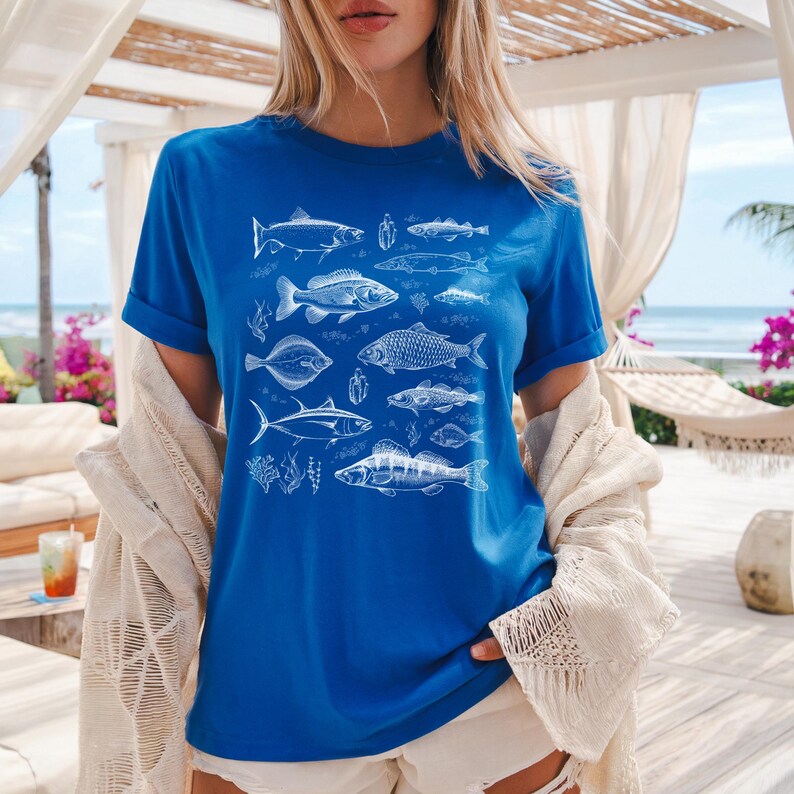 Puede incluir: Camiseta azul real con una ilustraci&oacute;n blanca de varias especies de peces. El dise&ntilde;o incluye dibujos detallados de diferentes peces, algas marinas y elementos acu&aacute;ticos. La camiseta tiene mangas cortas y un corte relajado.