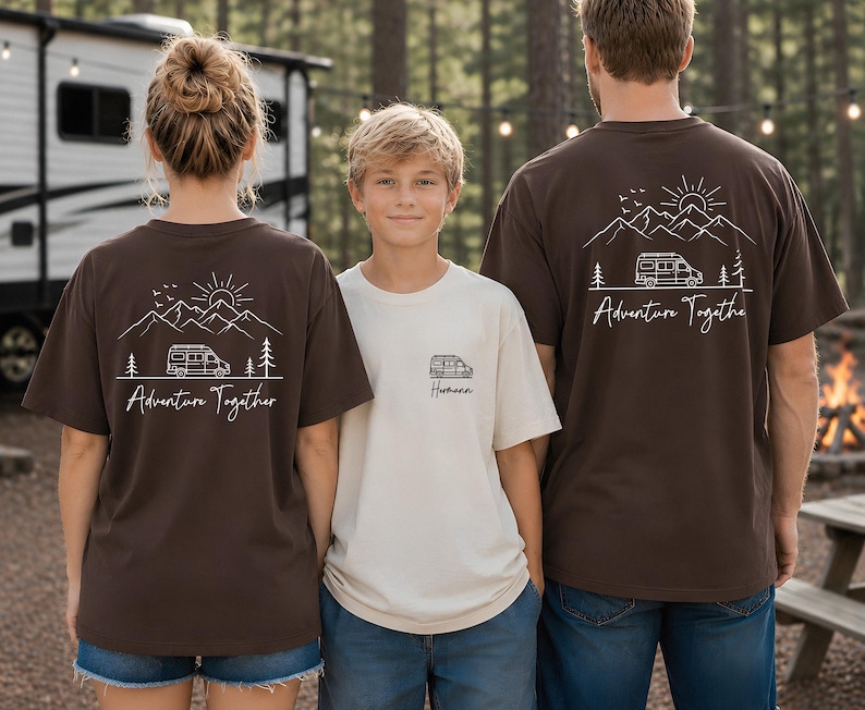 May include: Three people wearing matching t-shirts with a camping theme. The shirts are brown and cream-colored, featuring a mountain, sun, and camper van graphic with the words "Adventure Together" and "Hometown". The shirts are perfect for family camping trips.