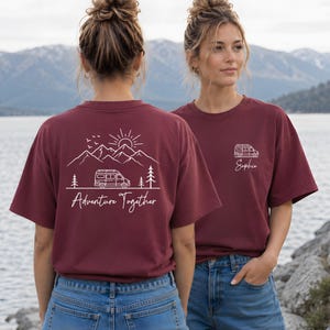 May include: Burgundy-colored t-shirts with white graphic designs. One shirt features a camper van, mountains, sun, trees, and the text "Adventure Together." The other shirt has a camper van and the name "Sophie."