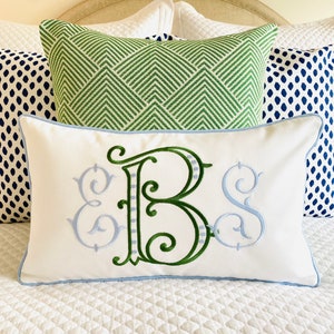 May include: A rectangular white throw pillow featuring an embroidered monogram with the letters E, B, and S. The central letter B is large and green, while the flanking E and S are smaller and light blue. The pillow has light blue piping edges.