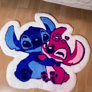 Pu&ograve; includere: Un tappeto bianco e soffice con un personaggio dei cartoni animati blu e rosa che si abbracciano. Il tappeto ha un bordo bianco ed &egrave; posto su un pavimento in legno. I personaggi sono in tonalit&agrave; di blu e rosa.