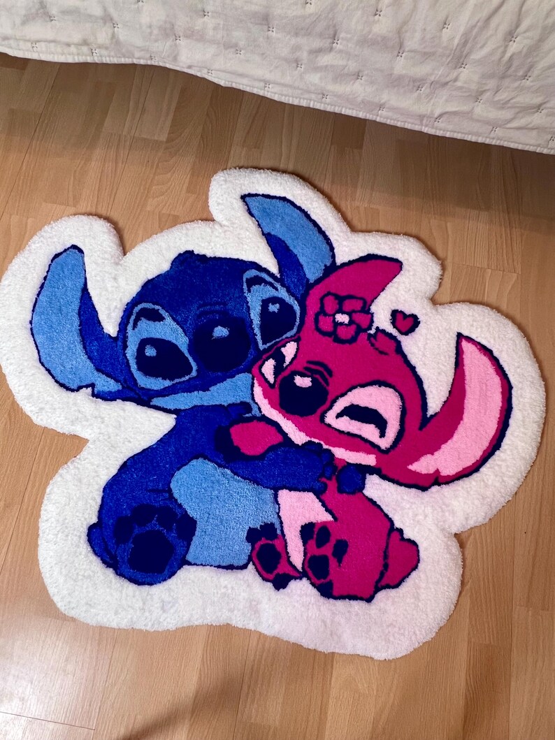 Pu&ograve; includere: Un tappeto bianco e soffice con un personaggio dei cartoni animati blu e rosa che si abbracciano. Il tappeto ha un bordo bianco ed &egrave; posto su un pavimento in legno. I personaggi sono in tonalit&agrave; di blu e rosa.