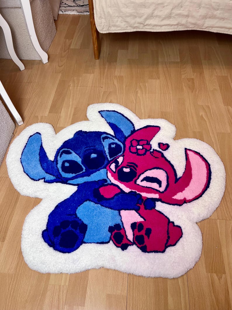 Pu&ograve; includere: Un tappeto bianco a forma di nuvola con un personaggio dei cartoni animati blu e rosa che si abbracciano. I personaggi si abbracciano, con il personaggio blu a sinistra e il personaggio rosa a destra. Il tappeto &egrave; su un pavimento di legno.