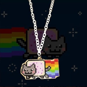 May include: A silver-toned chain necklace featuring a flat, pixelated pendant of a gray cat with a pink-spotted body, trailing a vibrant, multi-colored rainbow behind it. The pendant is suspended from a simple, polished metal link chain.
