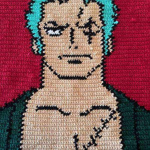 May include: Crocheted portrait of a character with teal hair, a scar over his left eye, and a stern expression. The character's skin is tan, with black outlines and details. The background is red, and the character's clothing is green.
