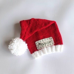 May include: Red and white knitted Santa hat with a white pom-pom and a name tag that says "Mason".