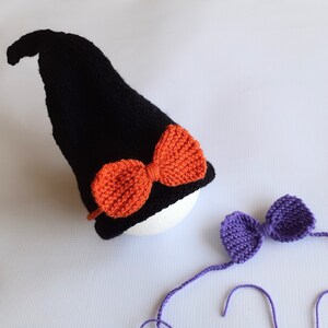 May include: A black knitted witch hat with an orange bow and a purple bow with long ties.