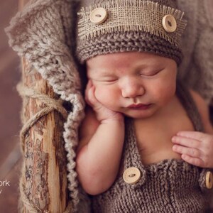 K&ouml;nnte beinhalten: Ein schlafendes Baby tr&auml;gt eine braune Strickm&uuml;tze mit einem Leinenband und Kn&ouml;pfen. Das Baby tr&auml;gt ein braunes Strickoutfit mit Kn&ouml;pfen. Das Baby liegt auf einer braunen Strickdecke.