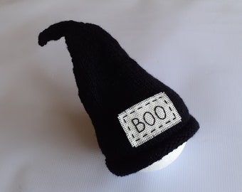 May include: Black knitted witch hat with a white felt patch that says "BOO!" in black embroidery.