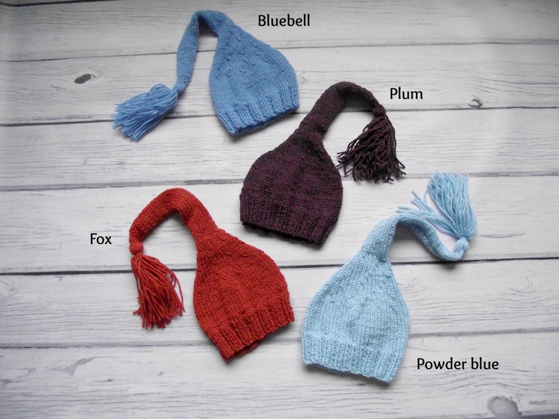 May include: Four knitted baby hats with long tails and tassels in the colors bluebell, plum, fox, and powder blue.