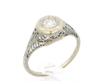 May include: A delicate filigree ring with a round, clear gemstone set in a hexagonal bezel. The ring is made of white gold and has a vintage style.