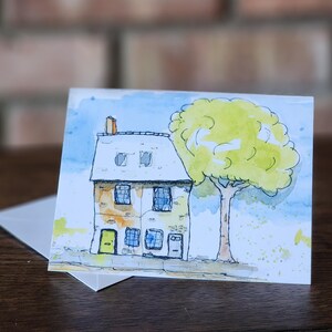May include: A watercolor painting of a small, two-story house with a yellow door and a green tree in front. The house has a white roof and brown brick walls. The tree has green leaves and a brown trunk.