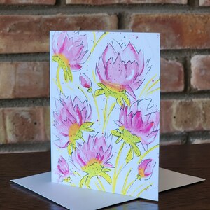 May include: A greeting card with a watercolor illustration of pink flowers with yellow stems and green leaves on a white background.