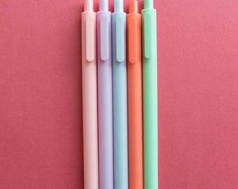May include: Five pastel colored pens lined up on a red background. The pens are pink, lavender, light blue, orange, and green.