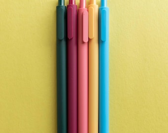 May include: Five colorful pens lined up on a yellow background. The pens are dark green, burgundy, light pink, yellow, and light blue.